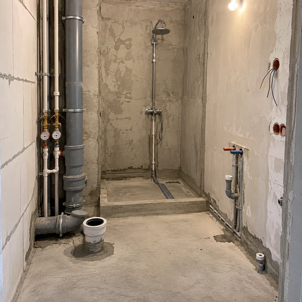 Łazienka w bloku z widocznymi instalacjami wodnymi, kanalizacyjnymi i elektrycznymi przed remontem